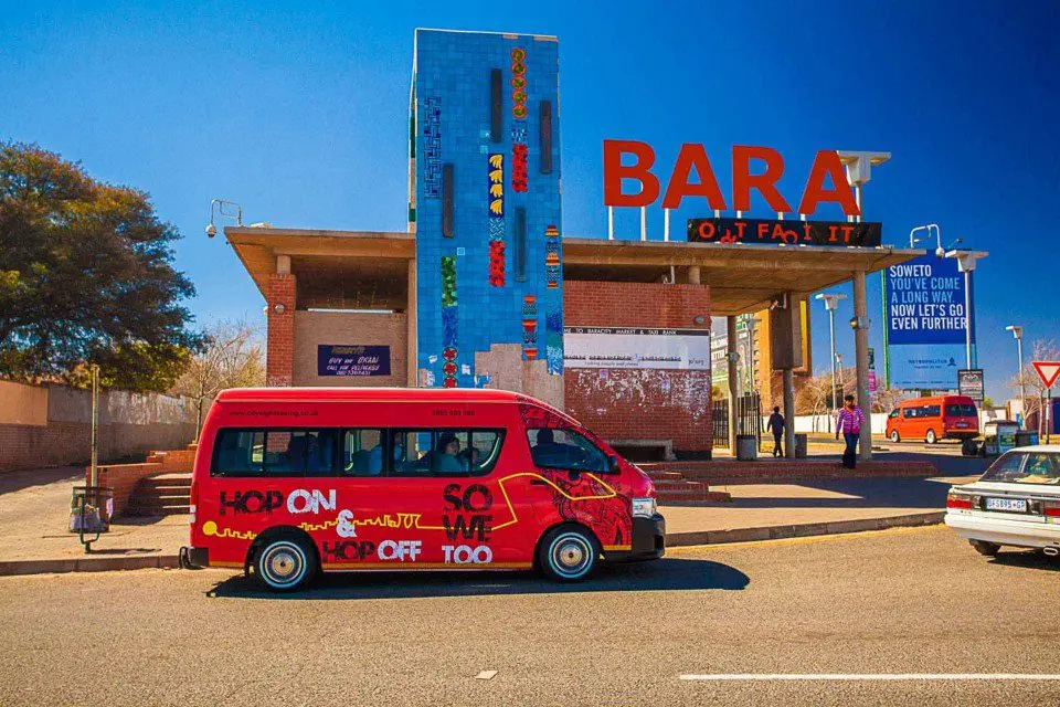 The City Sightseeing Joburg SO WE TOO Soweto tour bus caught from Gold Reef City in front of Bara sign