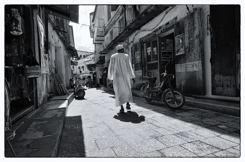 A man in a kanzu walking through Stone Town