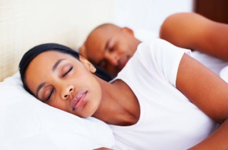 A woman with relaxed hair sleeping on a pillow with a man behind