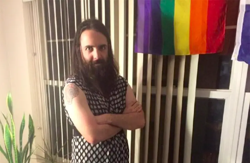 A bearded man in a dress with gay pride flag