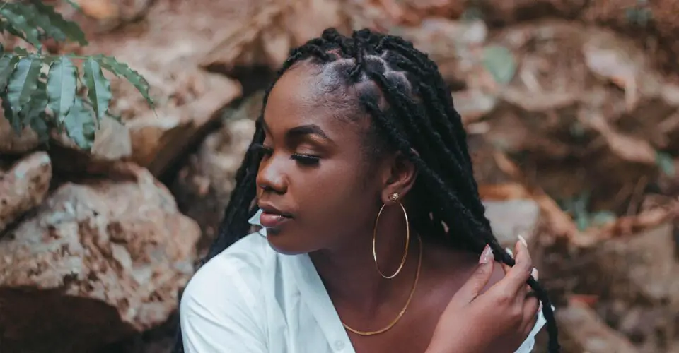 How to Retwist Your Own Locs: a dreadlocked woman sitting among rocks
